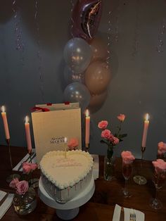 a birthday cake sitting on top of a table next to candles and flowers with balloons in the background