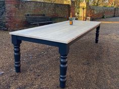 a wooden table sitting in the middle of a gravel field next to a brick wall