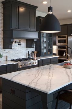 a kitchen with black cabinets and white marble counter tops, an island in the middle