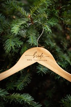 a wooden hanger with the name bride hanging from a pine tree in front of evergreen needles