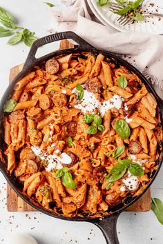 a skillet filled with pasta and sauce on top of a wooden cutting board