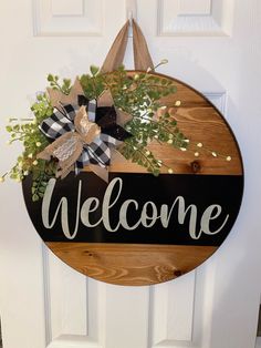 a welcome sign hanging on the front door with greenery and ribbon attached to it