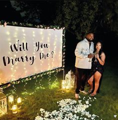 a man and woman standing in front of a sign that says will you marry me?