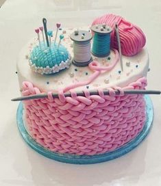 there is a cake that has yarn and knitting needles on top of it, along with two spools of thread