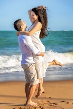 a man holding a woman on the beach while she holds her hair in the air