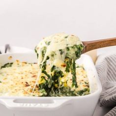 a casserole dish filled with spinach and cheese being lifted from the casserole