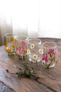 four glasses sitting on top of a wooden table with flowers painted on the glass cups