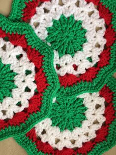 three crocheted coasters with green and red designs on them sitting on a table