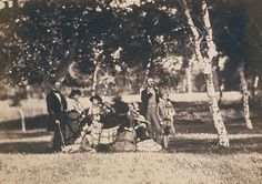 an old black and white photo of people sitting in the grass with trees behind them