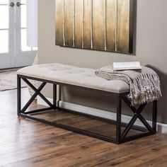 a bench sitting on top of a hard wood floor next to a wall with a painting above it