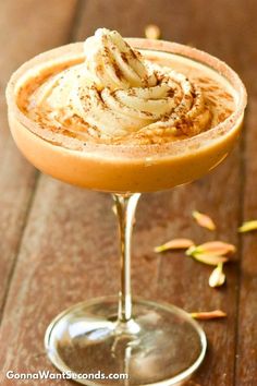 an orange drink with whipped cream on top in a coupe glass sitting on a wooden table