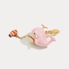 a pink and white whale shaped keychain hanging from a gold plated chain