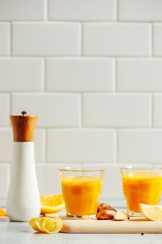 two glasses of orange juice on a cutting board with lemons and an orange peel