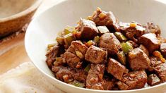 a white bowl filled with meat and vegetables on top of a wooden table next to bread