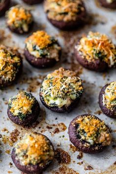 small appetizers with cheese and spinach sprinkled on them sitting on a baking sheet