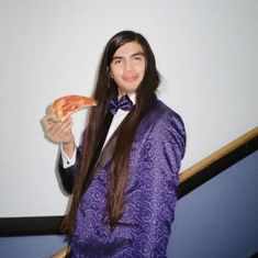 a man in a purple suit is holding a slice of pizza and posing for the camera