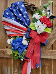 a patriotic wreath with flowers and an american flag ribbon hanging on a wooden fence in front of a door