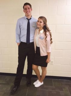 a man and woman standing next to each other in front of a white brick wall