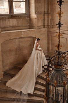 a woman in a wedding dress standing on some stairs next to a light fixture and lamp