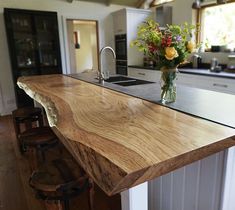 a wooden counter top in a kitchen next to a bar with stools and flowers