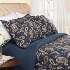 a bed with blue and gold comforters in a bedroom next to a white flower vase