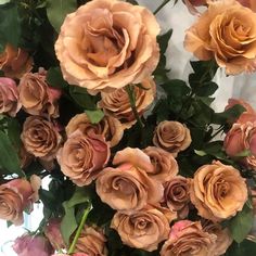 an arrangement of peach colored roses in a vase with green leaves and pink flowers on the stems