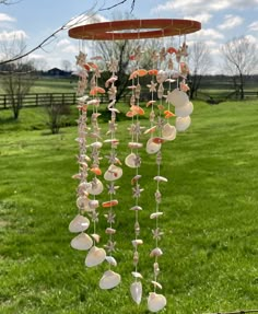 a wind chime with shells hanging from it's side in the grass near a tree