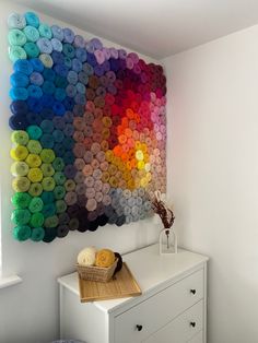 a white dresser topped with a basket filled with yarn next to a rainbow wall art