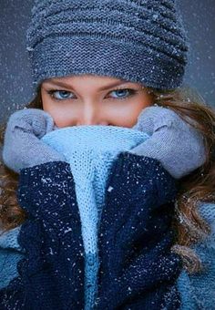 a woman covering her face with two hands while wearing winter clothes and mittens