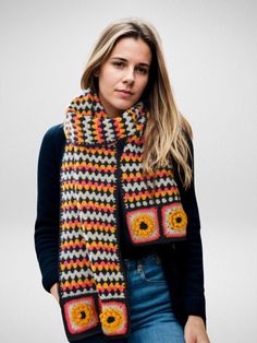 a woman wearing a multicolored crocheted scarf and matching mittens is standing in front of a white background