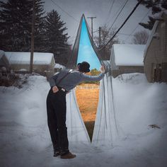 a man standing in front of a mirror with snow on the ground and houses behind him