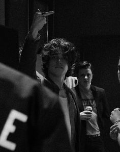 black and white photograph of three people standing in a room with one holding up a cell phone