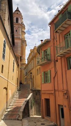 an alleyway with steps leading up to buildings and a clock tower in the background