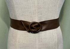 a brown leather belt on a mannequin's torso with a circular buckle