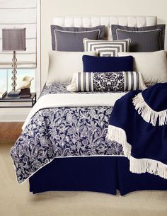 a bed with blue and white comforters, pillows and blankets on top of it