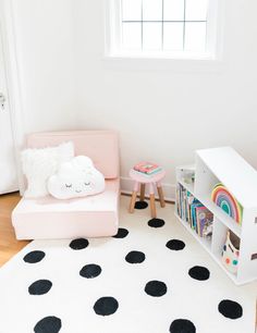 a child's room with black and white polka dots on the floor, bookshelf, and pink chair