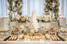 a white wedding cake surrounded by desserts and flowers