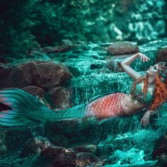 a woman with red hair is sitting on rocks in the water and has her hands behind her back