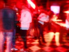 blurry photograph of people standing in a room with checkered floor and red lighting