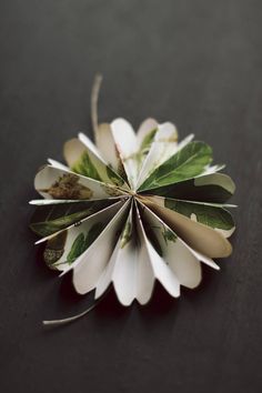 a close up of a paper flower on a black surface with white petals and green leaves