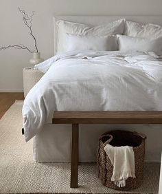 a bed with white linens and pillows in a small room next to a basket