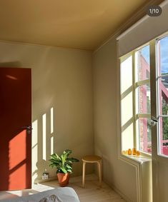 a bedroom with an open window and a plant in the corner