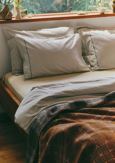 a bed with pillows and blankets in front of a window