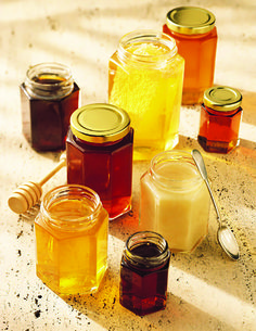 several jars filled with different types of honey sitting on a table next to spoons