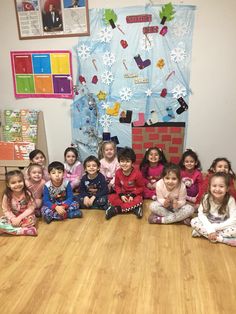 a group of children sitting on the floor in front of a bulletin board with christmas decorations