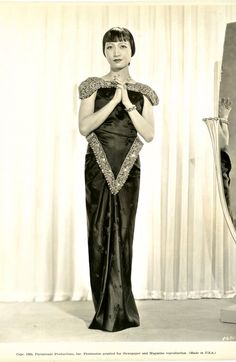 an old fashion photo of a woman in a black and white dress with her hands clasped