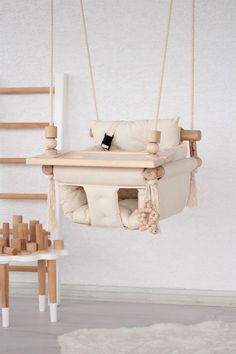 a swing chair hanging from the ceiling in front of a white wall and wooden ladders