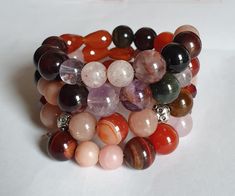 This is indeed an attractive eye candy. The crystals used in the making of this bracelet display the colors of fall - bright orange, russet red, pink and yellow. This unique memory bracelet comprises a medley of 10 mm carnelian, multi coloured tiger's eye, phantom amethyst and rose quartz crystals as well as 8 mm sunstone and garnet beads. It is accented with silver accents, Swarovski crystals and flower charms which gives it a fashionable outlook. A nice chunky piece of bracelet to have to brighten your plain attire or complement your gaudy ones,  This medley of crystals bracelet provides a burst of colour and complements any attire.   Fits a size 15 to 16 cm wrist. Handmade Orange Agate Bracelets, Handmade Orange Agate Bracelet, Handmade Carnelian Round Bead Bracelets, Handmade Orange Agate Beaded Bracelets, Handmade Spiritual Orange Stretch Bracelet, Handmade Wrap Bracelet With Round Beads For Healing, Handmade Carnelian Bracelets, Handmade Orange Crystal Bracelet Gift, Spiritual Multi-strand Beaded Bracelets As Gift