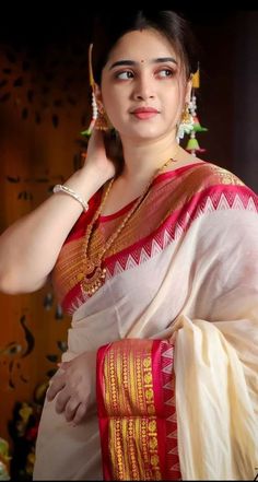 a woman in a white and red sari with gold jewelry on her neck is posing for the camera