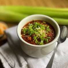 a white bowl filled with chili and garnish on top of a napkin next to celery